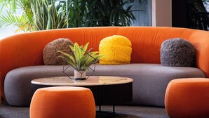 Een moderne woonkamer met een gebogen bank, oranje kussens en een ronde salontafel met een plant.