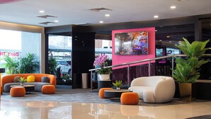 Een moderne lobby met een witte bank, oranje poefs, een bijzettafeltje en een groot schilderij aan de wand.