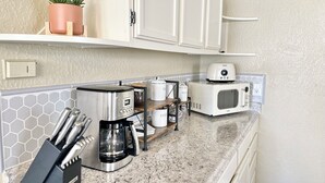 Une cuisine avec des meubles blancs, une machine à café, un four à micro-ondes et une plante en pot.