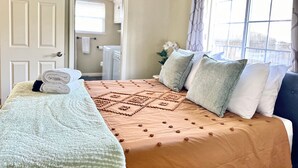 Un lit bien fait, avec une couvre-lit à motifs et des oreillers, une fenêtre avec des rideaux et une porte donnant sur une autre pièce.
