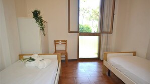Una habitación con dos camas individuales, una silla de madera, un armario blanco y una ventana con vistas a zonas verdes.