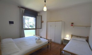 A room with two single beds, a wardrobe, a small bedside table with a lamp, and a window with curtains. - Comfortable Flat With Balcony for Nine Guests in Lignano Sabbiadoro (Lignano Sabbiadoro)