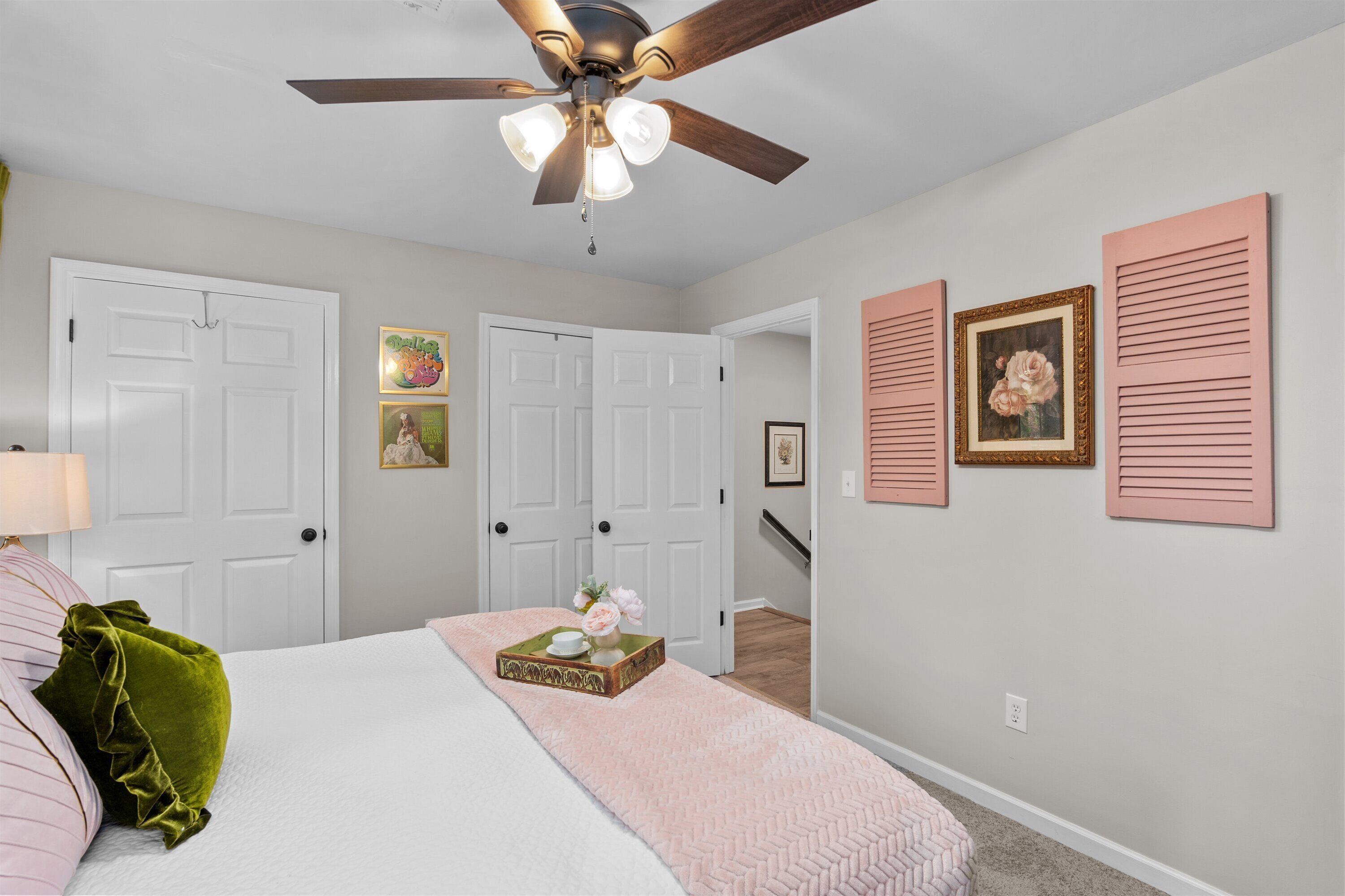 A bedroom with a bed, a ceiling fan, two doors, and wall-mounted artwork.