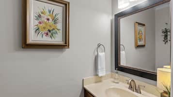 A bathroom with a large mirror, a framed floral artwork, a towel ring, and a sink with a soap dispenser.