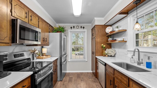 A modern kitchen with wooden cabinets, stainless steel appliances, and a window with blinds.