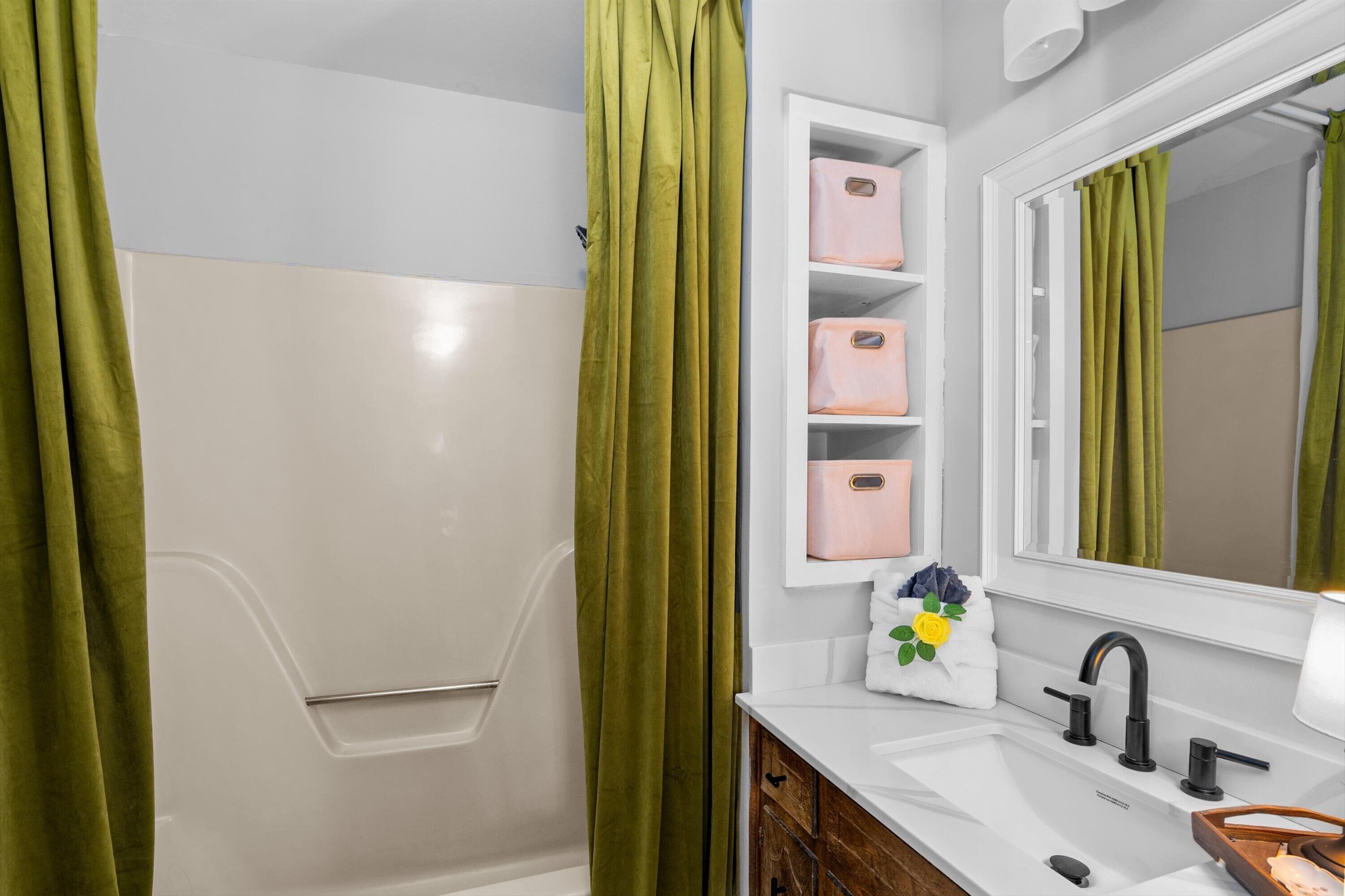 A bathroom with a white bathtub, green shower curtains, a white sink with black faucets, and a mirror above the sink.