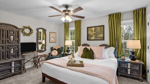A bedroom with a bed, a dresser, a television, a ceiling fan, and green curtains.