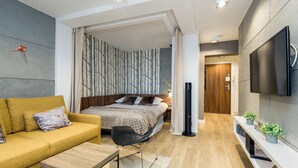 A modern bedroom with a bed, a sofa, a TV, and a console table with plants. - Apartament Spodek - by Kairos Apartments (Katowice)