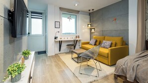 A modern living room with a sofa, a chair, a TV, a window, and a small table. - Apartament Spodek - by Kairos Apartments (Katowice)