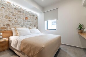 A bedroom with a stone wall, a bed with white bedding, a nightstand, a window with a view, and a plant on a shelf.