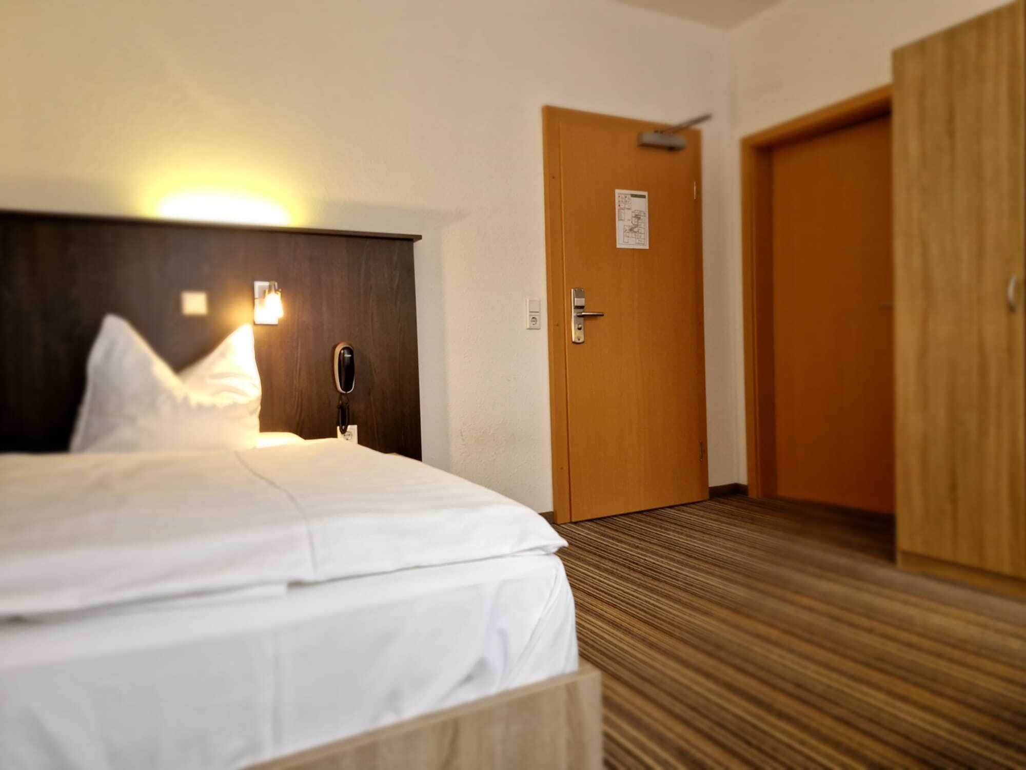 A hotel room with a bed, a bedside lamp, a phone, and a door.