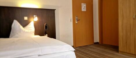 Habitación de hotel con una cama, una lámpara de noche, un teléfono y una puerta.