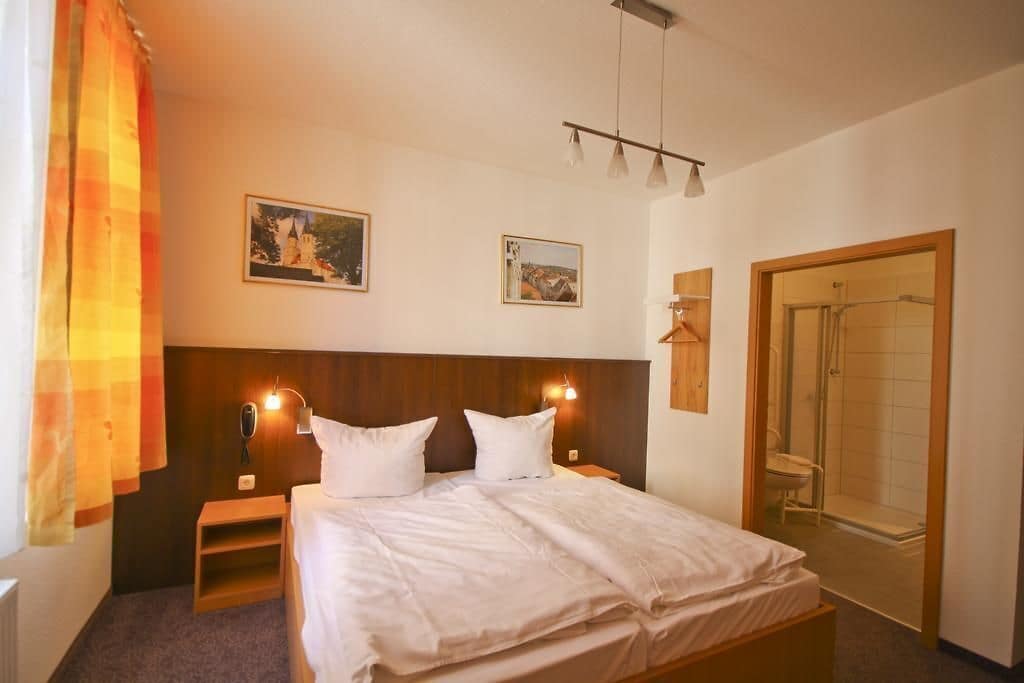 Ein Hotelzimmer mit einem Bett, Nachttischen, einer Dusche und zwei Bildern an der Wand.