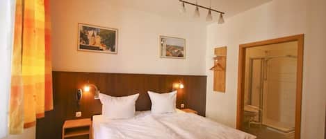 Habitación de hotel con cama, mesitas de noche, ducha y dos cuadros colgados.