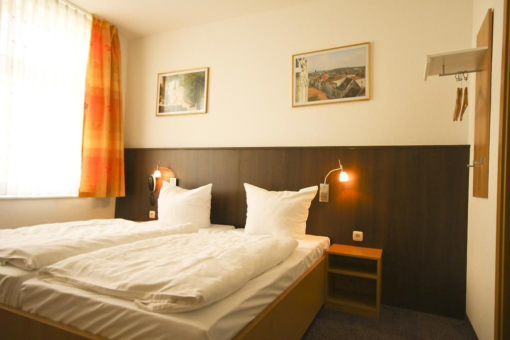 Habitación de hotel con una cama grande, dos mesitas de noche y dos lámparas de pared.