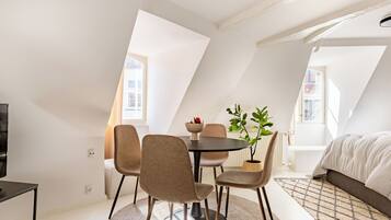 Una habitación moderna y luminosa con una mesa de comedor, cuatro sillas, una planta en maceta y una cama.