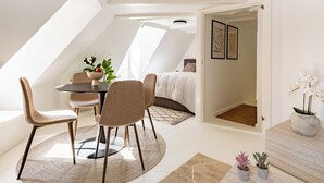 A modern loft bedroom with a skylight, a dining area with a round table and chairs, and a small balcony with potted plants. - Admiral - Cosy 1-bdr Apt in Central Copenhagen (Copenhagen)