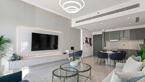 Un salon moderne doté d’un grand téléviseur à écran plat, d’une table basse en verre et d’un coin repas avec une table ronde et des chaises.