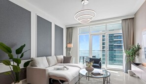 Relax in a contemporary living space with a light-colored sofa, glass coffee table, and floor lamp, offering a view of the city from the balcony.