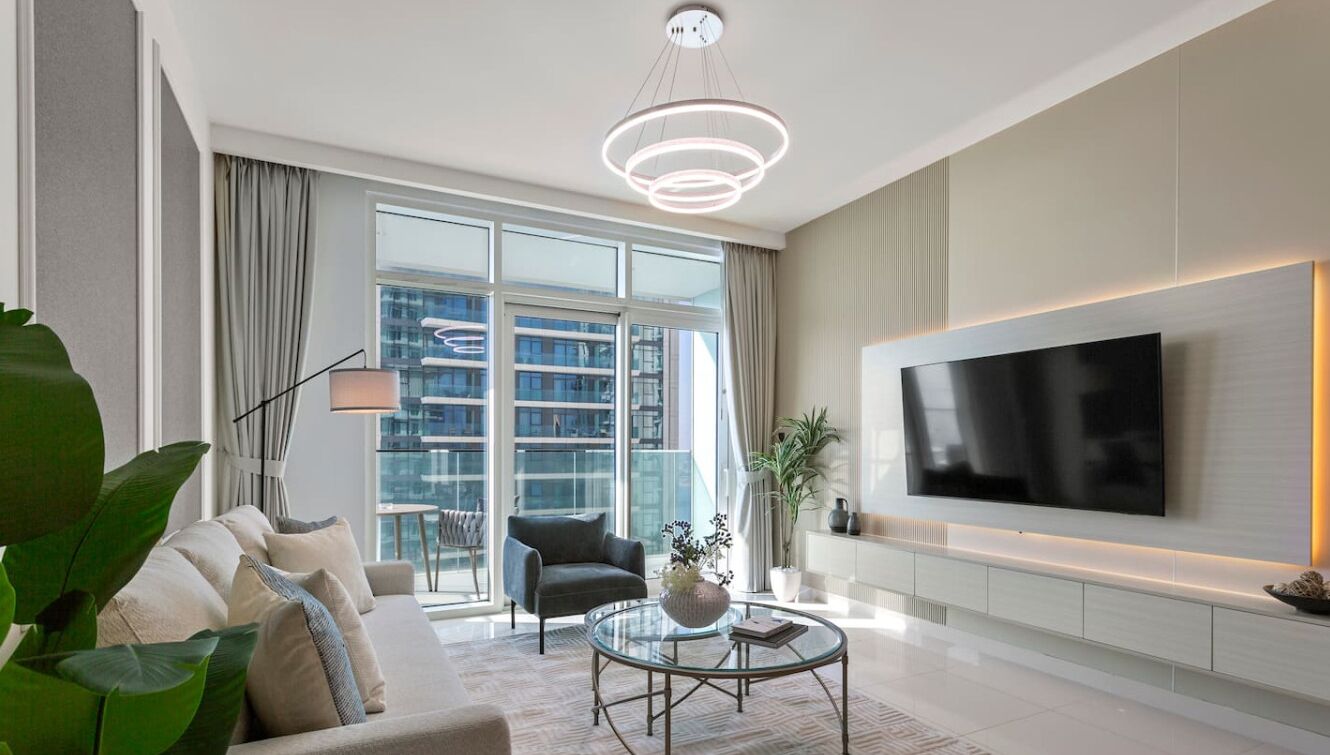 Ein modernes Wohnzimmer mit einem großen Flachbildfernseher an der Wand, einer bequemen Couch, einem Glastisch und einem großen Fenster mit Blick auf die Stadt.