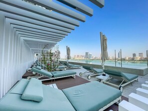 Relax on sunbeds with city skyline views, surrounded by umbrellas and a small table.