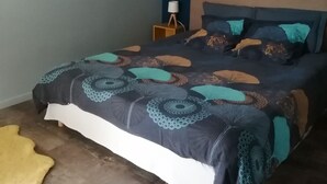 A bedroom with a bed, a bedside table with a lamp, a wall art piece, and a yellow rug.