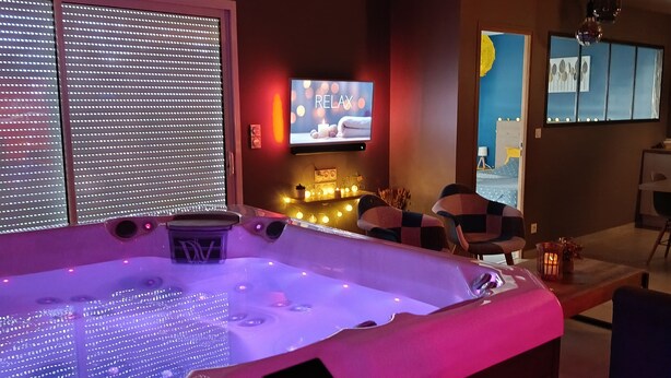 A modern spa room with a heated tub, a television, and ambient lighting.