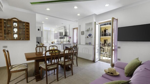 A modern living room with a dining area, a sofa, and a TV mounted on the wall. - ROSE SORRENTO HOUSE (Sorrento)
