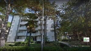 Ένα πολυώροφο κτίριο με μπαλκόνια, περιτριγυρισμένο από δέντρα και πρασινάδα.
