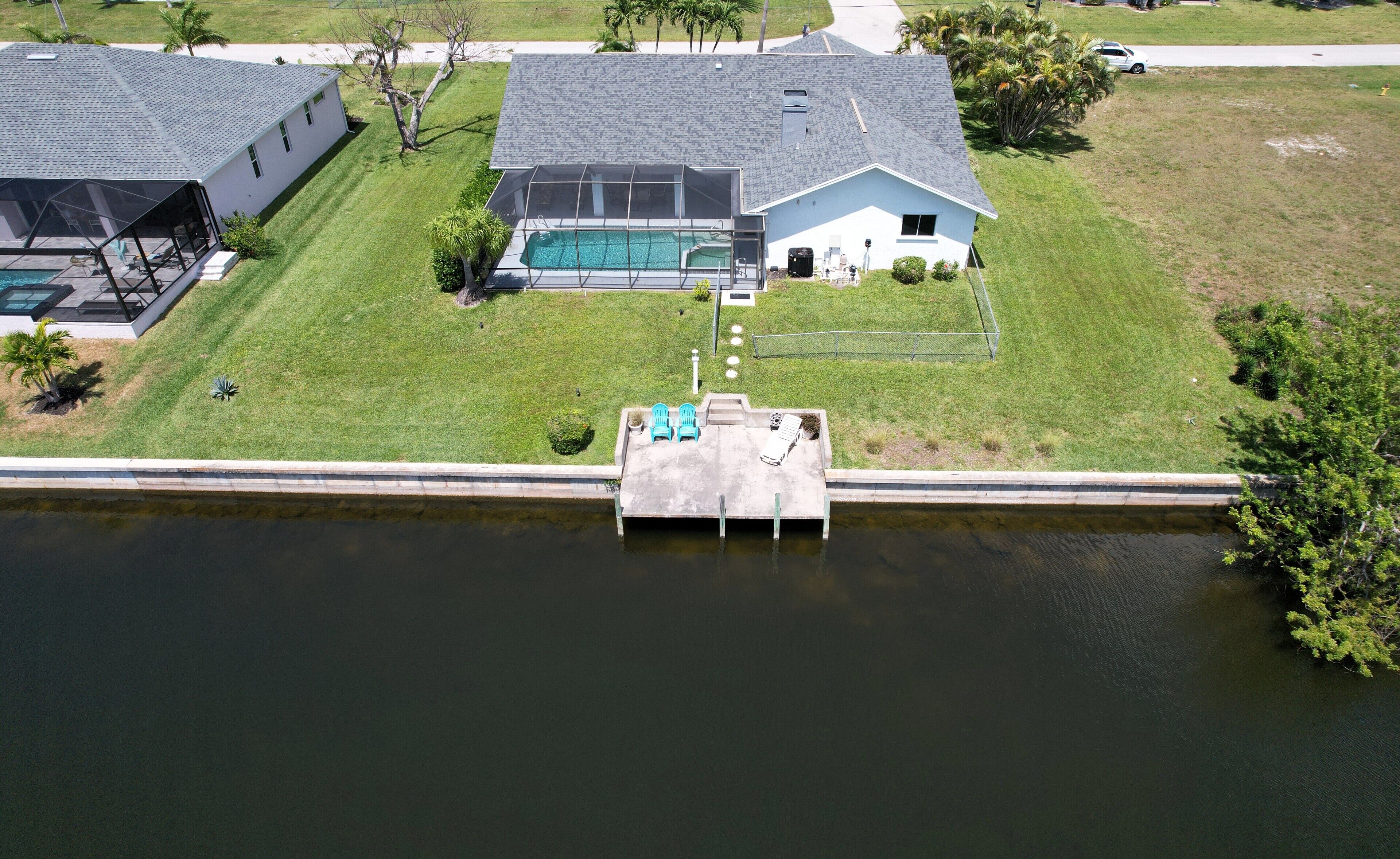 An aerial view of a residential property with a swimming pool, a dock, and a grassy yard.