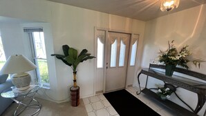 A room with a sofa, a lamp, a potted plant, a console table with a vase of flowers, and a door with decorative glass panels.