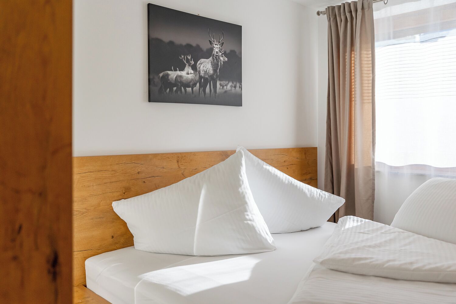 Ein ordentlich bezogenes Bett mit weißen Leinen und Kissen, ein hölzerner Kopfteil und ein gerahmtes Bild von Hirschen an der Wand.