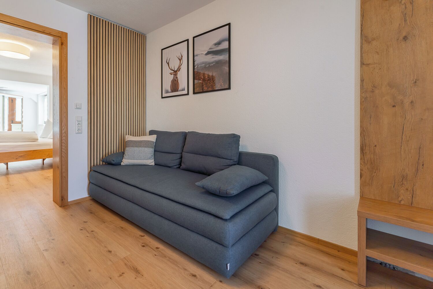 Una sala de estar moderna con un sofá gris, listones de madera y dos cuadros en la pared.