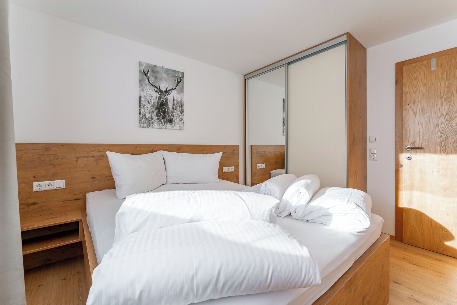 Una camera da letto con testiera in legno, biancheria bianca, un grande specchio e una porta con cornice in legno.
