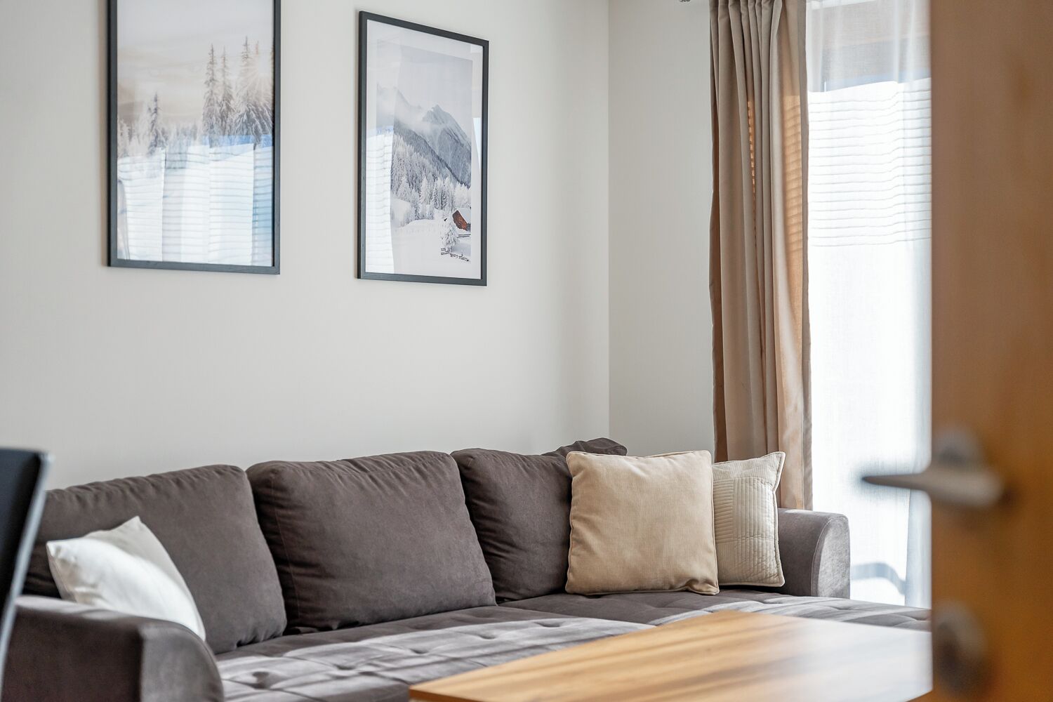 A modern living room with a grey sofa, a wooden coffee table, and two framed pictures on the wall.