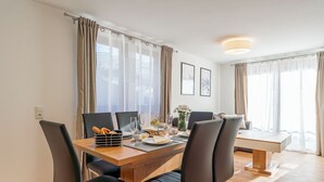 Ein moderner Essbereich mit einem Holztisch, schwarzen Stühlen und einer Bank. Vorhanden sind Vorhänge, eine Vase mit Blumen und ein gerahmtes Bild an der Wand.