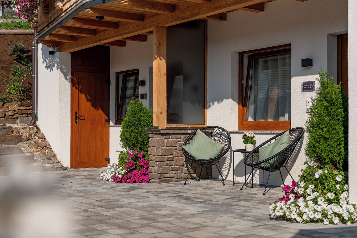 A cozy outdoor seating area with two chairs and a table, surrounded by potted plants and flowers.