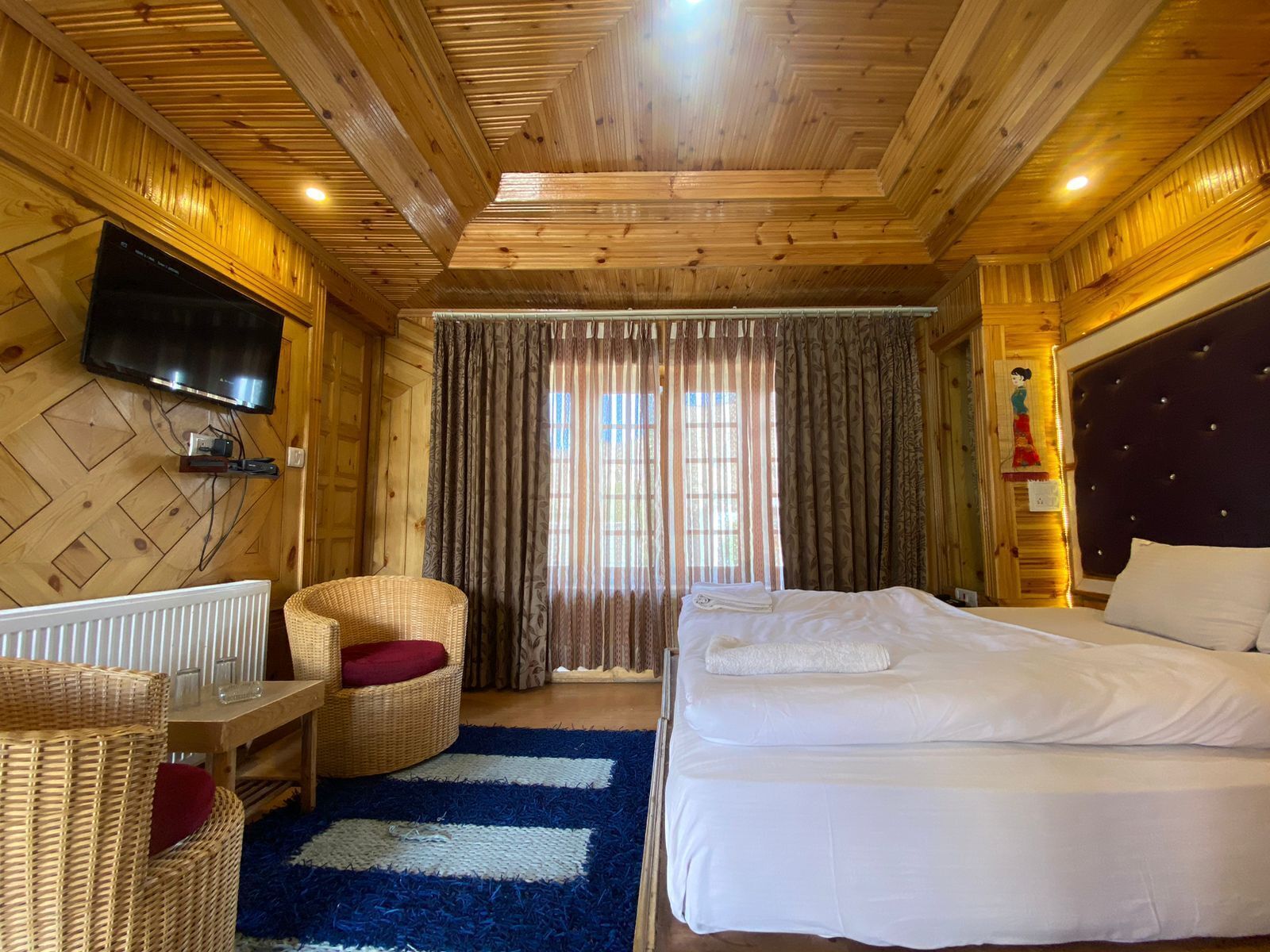 Une pièce en bois avec un lit, une télévision, une chaise et une fenêtre avec des rideaux.