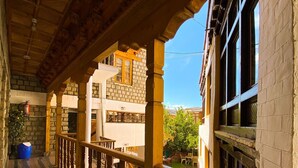 Un espacio al aire libre techado con barandillas de madera, un muro de piedra y vistas a un edificio con ventana y puerta.