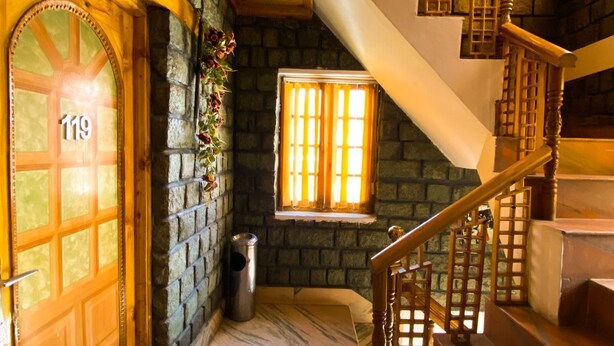 Una escalera de madera con un muro de piedra y una ventana con cortinas.