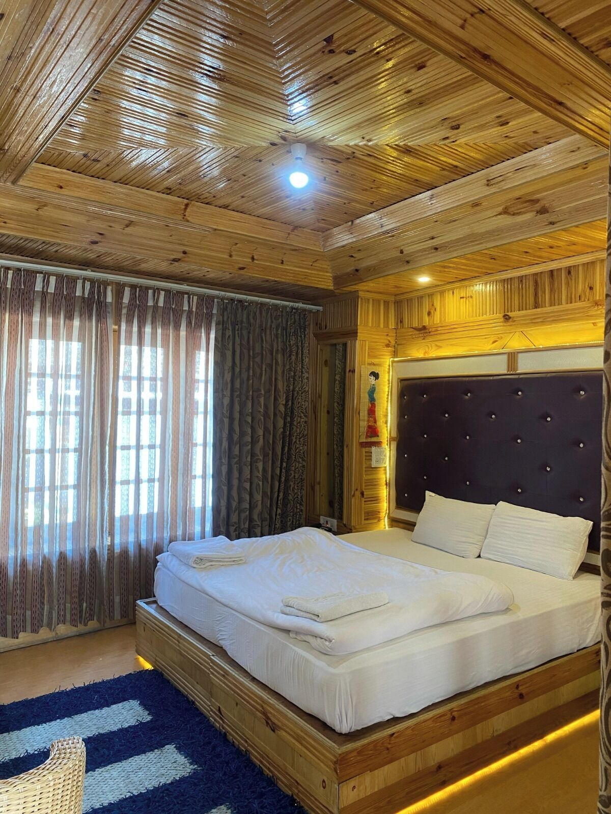 Una habitación con paneles de madera, una cama grande, un cabecero y una ventana con cortinas.