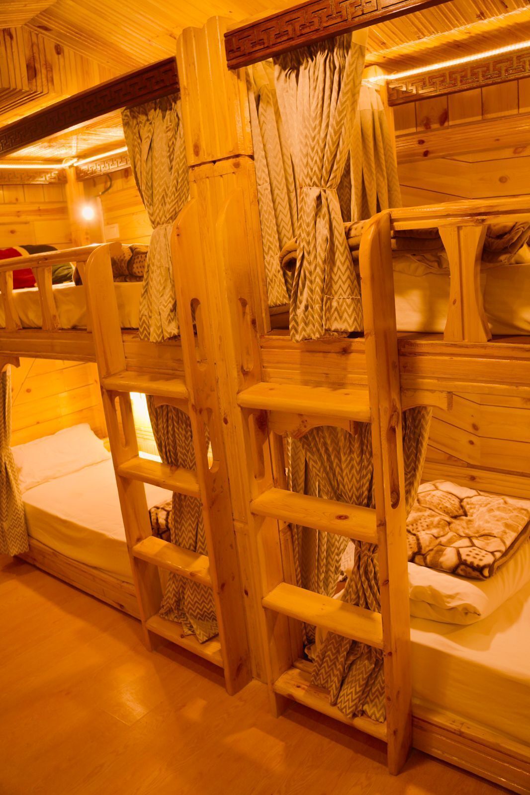 A cabin-style room with wooden bunk beds, a ladder, and curtains.