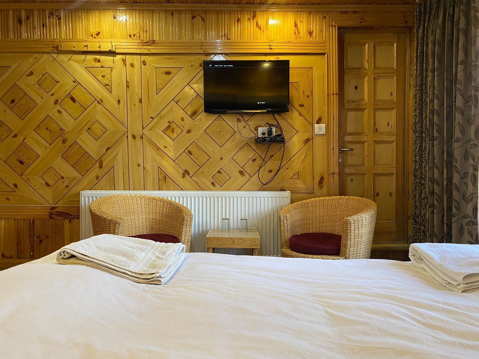 Habitación de hotel con una cama, dos sillones de mimbre, un televisor y un radiador.