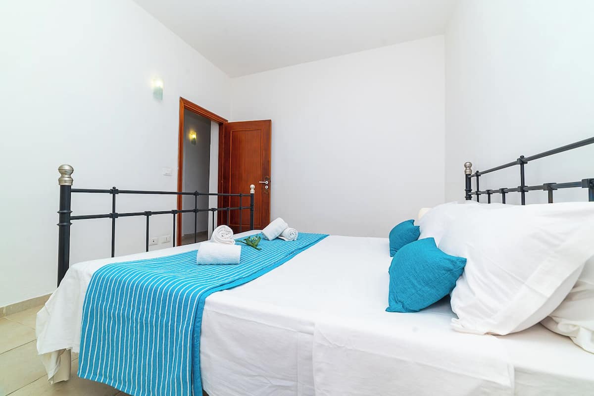 A single bed with a metal frame, white bedding, and blue striped and solid pillows.