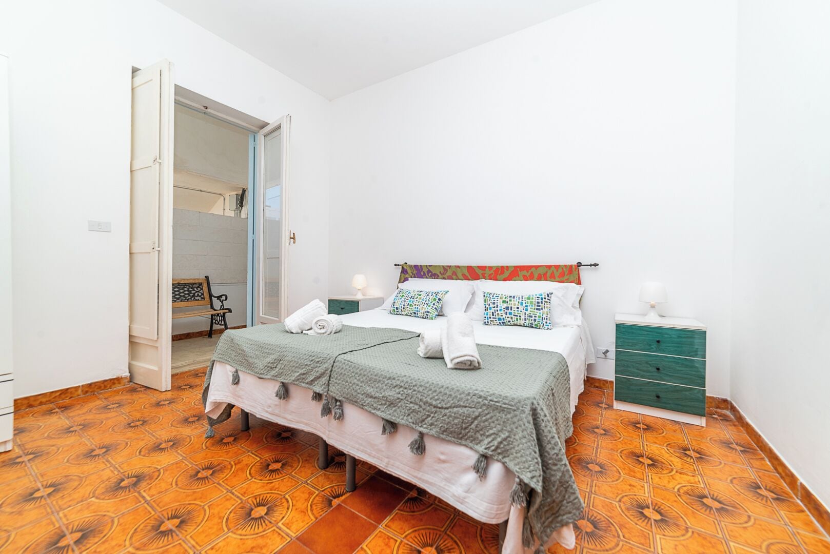 A bedroom with a bed, a nightstand, a dresser, and a door leading to another room.