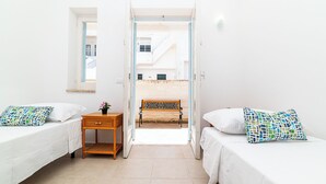 A room with two single beds, a small wooden nightstand with a plant, and a bench in the doorway. - Residence degli Oleandri (Villanova)