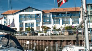 A marina with boats, a building with blue balconies, and a flag. - Charming 2-room apartment with pool in Hendaye, near port (Hendaye)