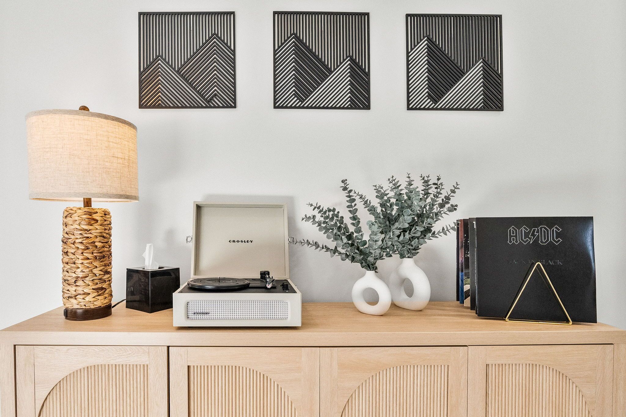 Un escritorio de madera con una lámpara, una radio Crosley, un florero con follaje y la portada de un disco de AC/DC.