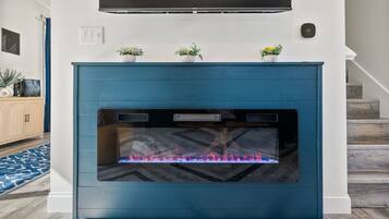 A modern fireplace with a blue facade, a flat-screen TV mounted above, and three potted plants on the mantel.