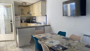A compact kitchen with a dining area, a TV mounted on the wall, and a view of the outside through a sliding door. - Family home near beach with WiFi and pets allowed (La Tranche-sur-Mer)
